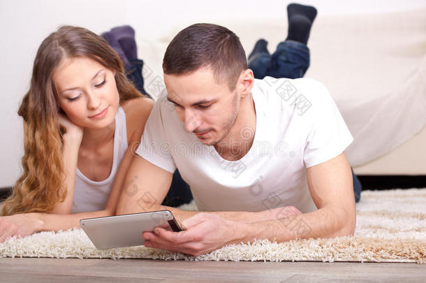 一对夫妇躺在地毯上看着平板电脑