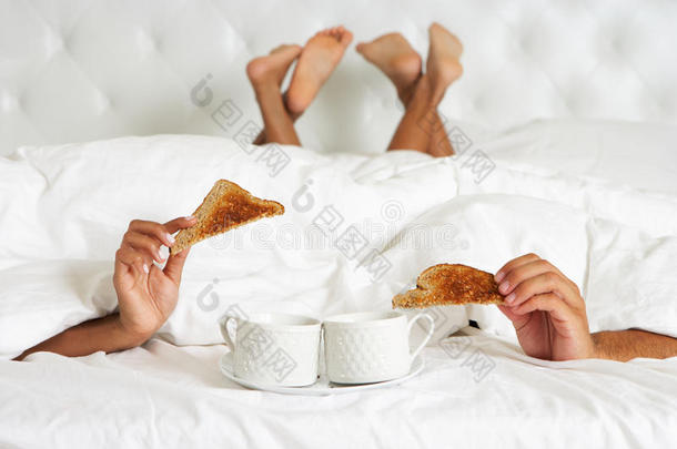 一对躲在羽绒被下的夫妇在床上享用早餐