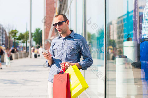 年轻人手里拿着许多彩色购物袋在商场购物。他拿着一部电话。