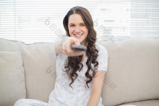 微笑的年轻女子拿着遥控器坐在舒适的沙发上