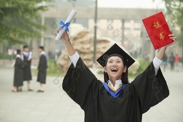 年轻的女大学毕业生，举起手臂举着文凭