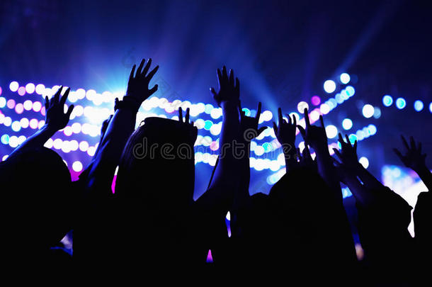 观众观看摇滚表演，手举在空中，后视图，舞台灯光