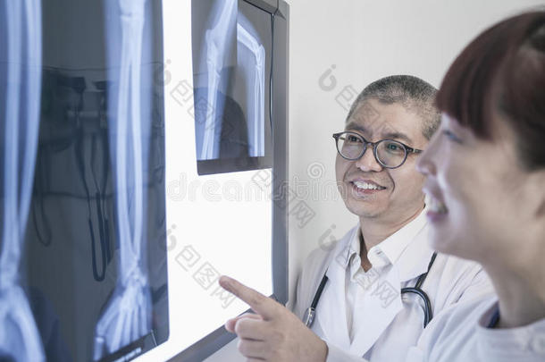 两个面带微笑的<strong>医</strong>生看着人体骨骼的x<strong>光片</strong>，指着