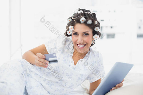 微笑的<strong>深色</strong>头发卷发者躺在床上用平板电脑在网上<strong>购物</strong>