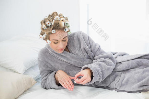 集中放松的金发女人在卷发器上涂指甲油