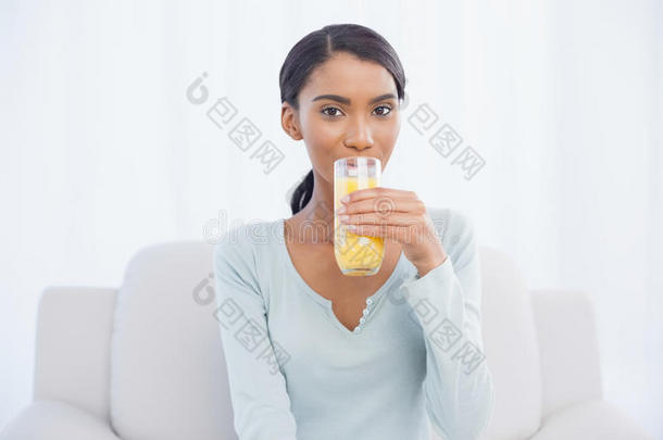 微笑的女人坐在舒适的沙发上喝橙汁