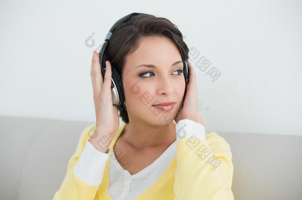 体贴的浅褐色黄色开襟衫，戴着耳机听音乐