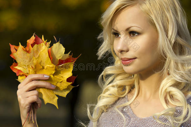秋季时尚女郎。金发碧眼的年轻女子，手里拿着黄色的枫叶。在外面。