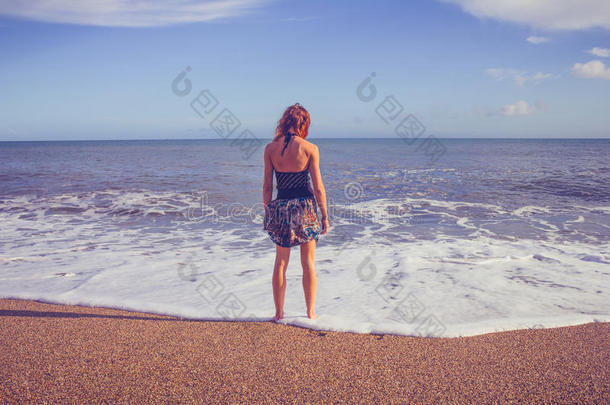 站在沙滩上看海的年轻女子的后视图