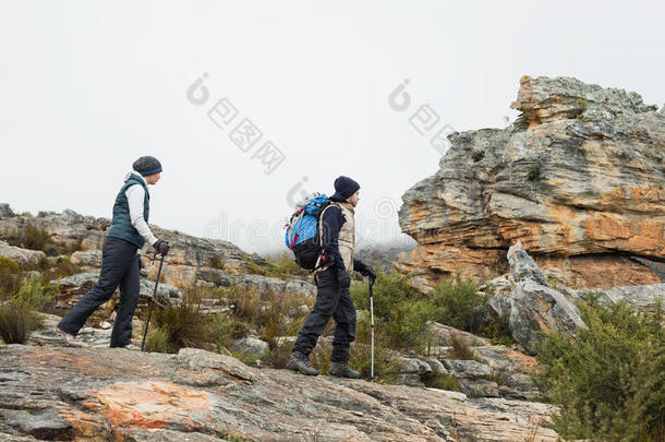 一对夫妇在岩石景观中穿行，在天空中用<strong>登山杖</strong>攀爬
