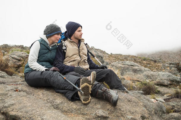 一对夫妇坐在岩石上，背着背包，拄着<strong>登山杖</strong>
