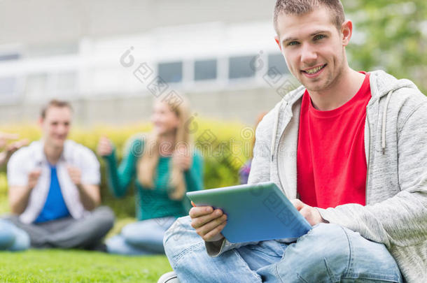 微笑的大学生抱着平板电脑和学生们在公园里