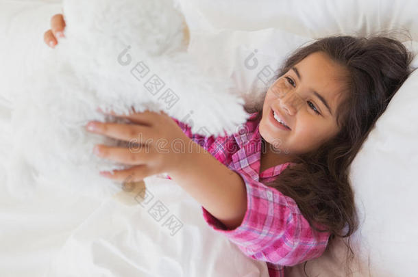 笑眯眯的女孩抱着毛绒玩具躺在床上
