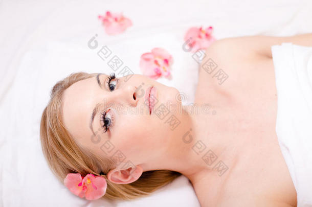 美丽的年轻迷人的金发女人的画像，在水疗过程中躺在花丛中放松