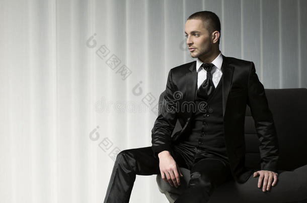 穿着燕尾服坐在沙发上的优雅的年轻<strong>时尚男士</strong>