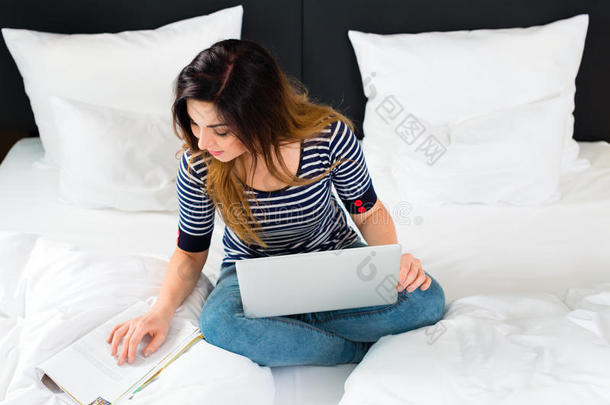酒店里的年轻女子躺在床上用无线网络和电脑上网