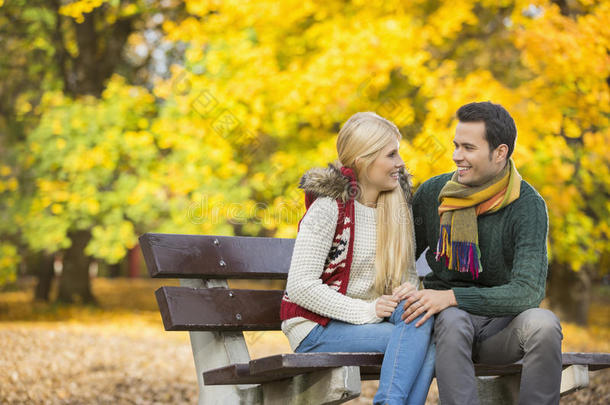 秋天，一对幸福的年轻夫妇坐在公园的长椅上看着对方