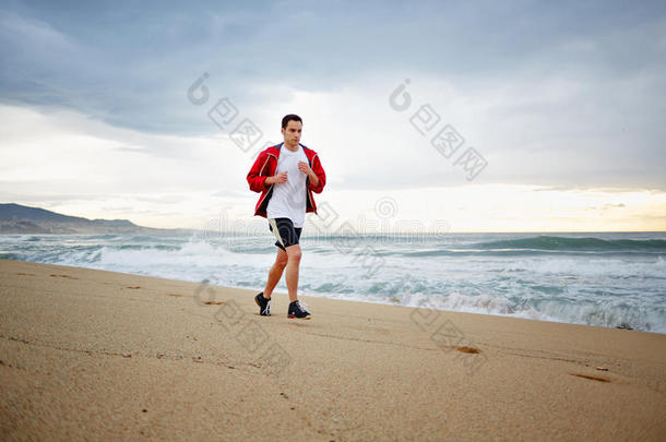 穿着红色<strong>风衣</strong>的年轻漂亮跑步者在美丽的海景下沿着海滩奔跑