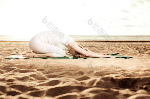 日出时，年轻美丽的苗条女人在海滩上练习瑜伽。日落瑜伽