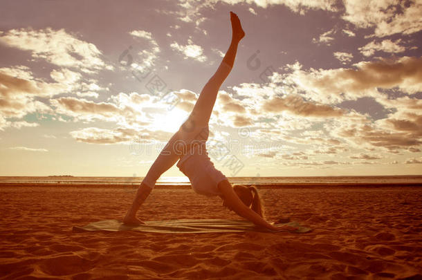 年轻美丽的苗条女人剪影练习瑜伽在海滩日落。日出瑜伽
