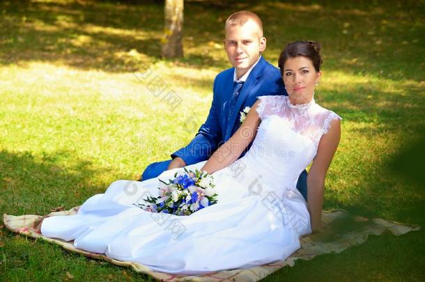 婚礼上幸福的新郎新娘坐在公园的草地上