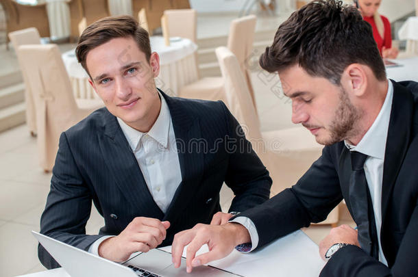 聪明的工作。两个成功而自信的商人穿着<strong>盛装</strong>坐在一间商务办公室的桌子旁
