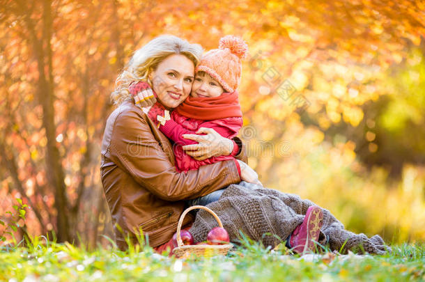 母亲和孩子坐在一起拥抱在秋天公园。