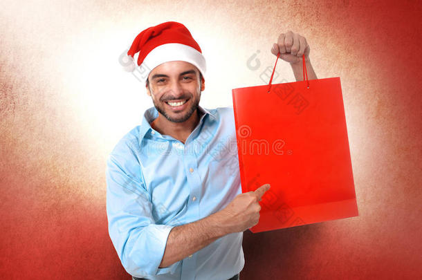 快乐的年轻帅哥戴着圣诞帽拿着红色的购物袋