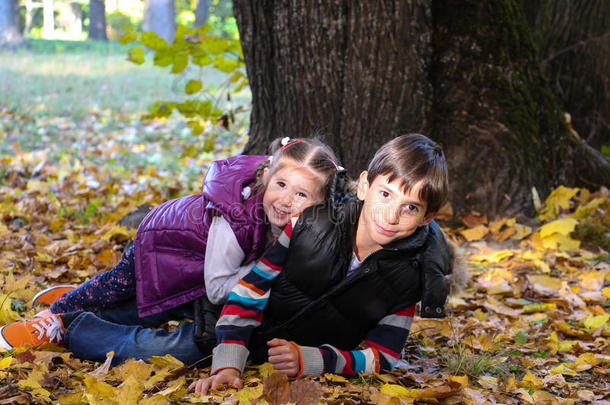 阳光明媚的秋天公园里，男孩和女孩坐在树叶上