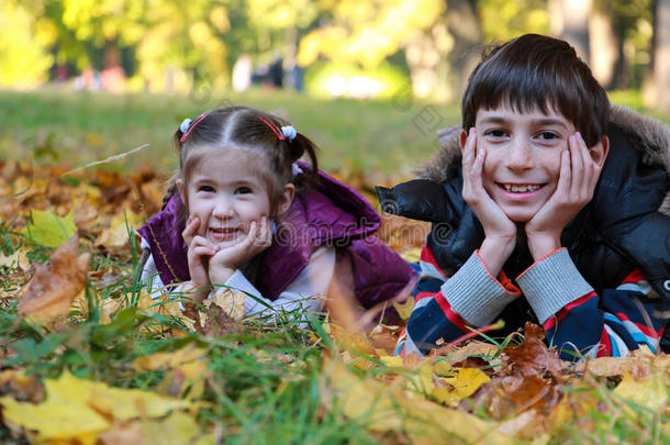 阳光明媚的秋天公园里，男孩和女孩坐在树叶上