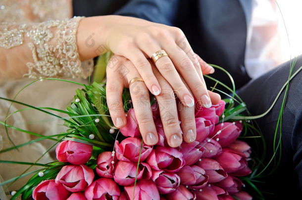 手拿戒指新娘和新郎在婚礼的粉色花束上