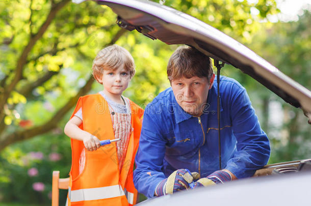 年轻的父亲教他的小儿子在家用汽车里换机油