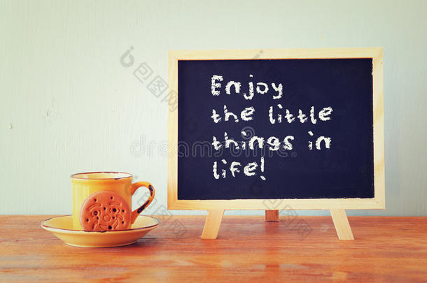 黑板上写着“享受生活中的点点滴滴”，旁边的咖啡杯放在木桌上