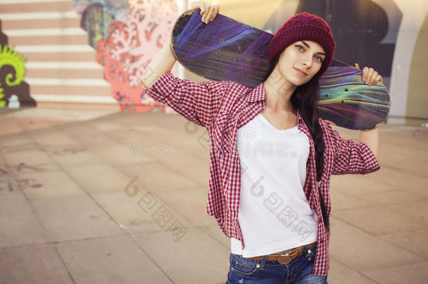 黑发少女穿着时髦的服装（牛仔<strong>裤</strong>短<strong>裤</strong>，短<strong>裤</strong>，格子衬衫，帽子），在公园里玩滑板