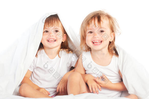 快乐的小女孩双胞胎妹妹在床上的毯子下玩得很开心