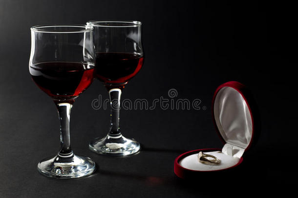 金戒指在珠宝盒和两个杯子装满红酒隔离在黑色