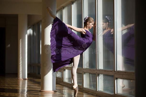 优雅的芭蕾舞演员穿着紫色连衣裙跳舞，腿高<strong>高举</strong>起，圣