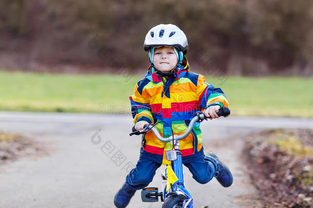 有趣可爱的学龄前儿童戴着安全帽，穿着五颜六色的雨衣骑着他的第一辆自行车