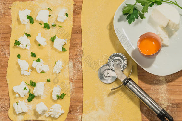 手工<strong>馄饨</strong>面团与新鲜鸡蛋，奶酪，欧芹和车轮面团切割机放置在木制桌子上。