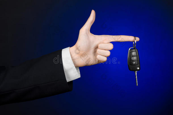 商业和礼物主题：穿着黑色西装的汽车推销员在工作室的深蓝色背景上拿着一辆新车的钥匙