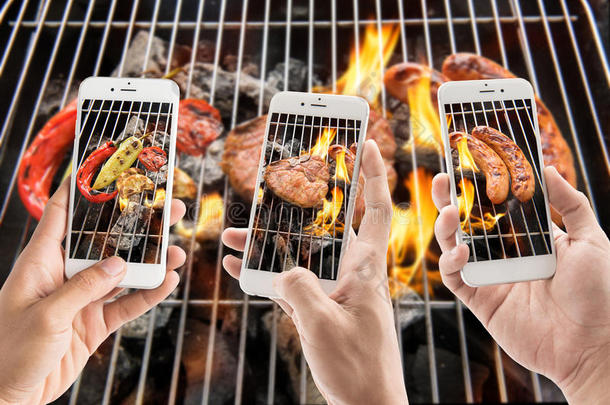 朋友们用智能手机在燃烧的烤架上拍香肠、猪排和蔬菜的照片