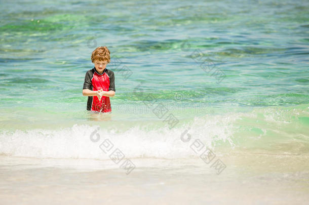 可爱的7岁男孩穿着红色的鲁西<strong>西游</strong>泳衣在热带海滩与白沙和绿色的海洋