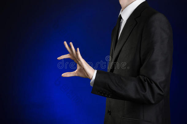 商人和手势主题：一个穿着黑色西装和白色衬衫的人在工作室的深<strong>蓝色</strong>背景上<strong>展示</strong>了一只手捏