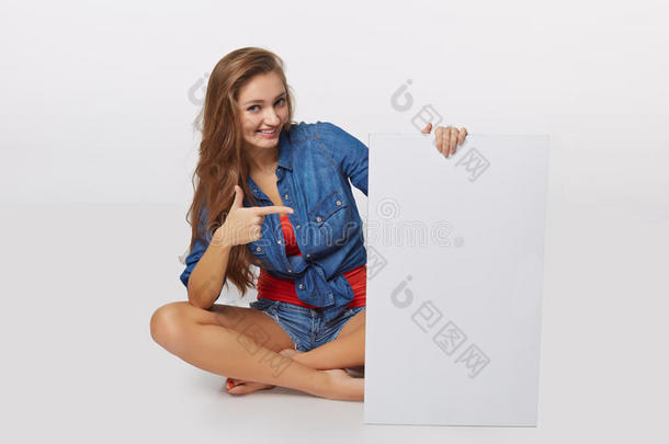 牛仔风格的肖像少女在地板上手持白色空白广告板横幅，白色背景