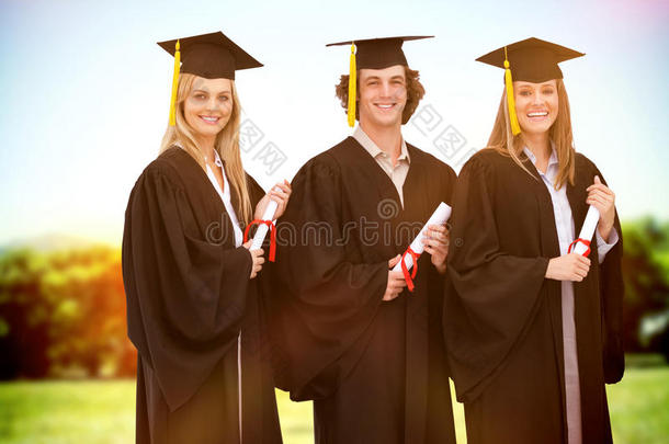 三个微笑的学生穿着研究生长袍拿着文凭的复合形象