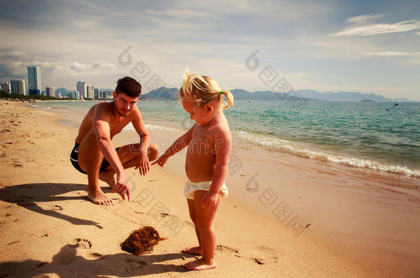 父亲在沙滩上给小女儿看海藻