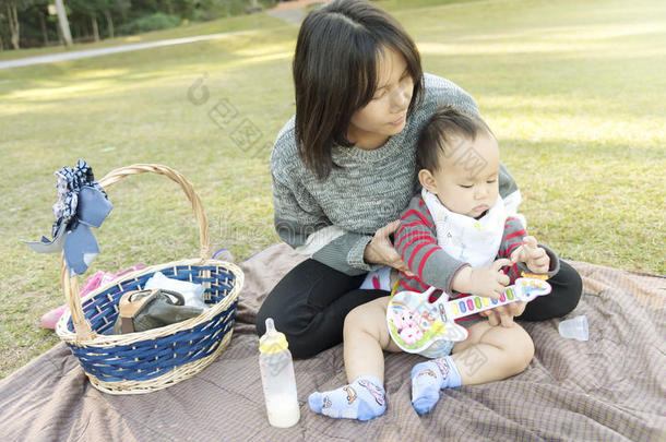 当家人在公园野餐时，亚洲母亲抱着孩子