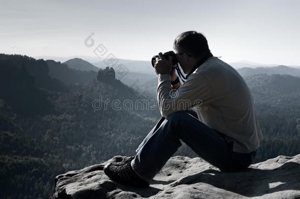 黑发男子正在日出时用大镜子相机在山顶的脖子上拍照。