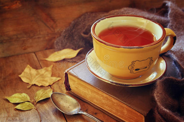 一杯带着旧书的茶，秋天的树叶和一条温暖的围巾放在木桌上