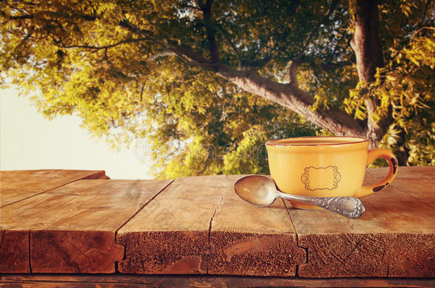 咖啡杯在木桌上的正面形象和森林背景前的秋叶。 复古风格的形象